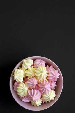 Mini meringues siyah arka plan, üstten görünüm üzerinde pembe bir kase. Yukarıdan, yükünü görüntüleyin. Yakın çekim. Kopya alanı.
