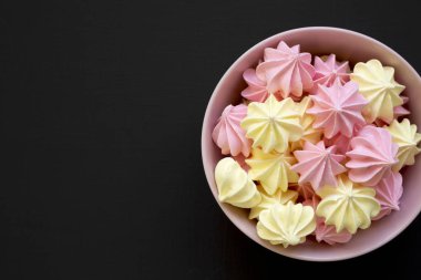 Mini meringues siyah arka plan, üstten görünüm üzerinde pembe bir kase. Yukarıdan görünüm üst. Yakın çekim. Metin için yer.