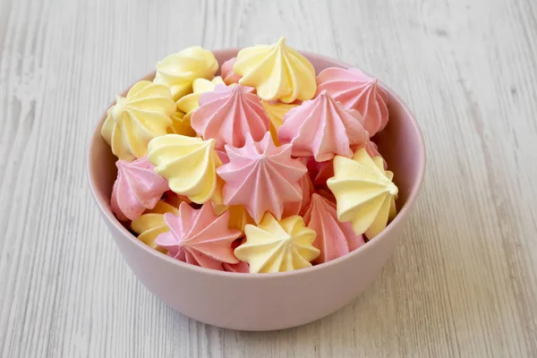 Mini meringues Beyaz ahşap arka plan, yan görünüm üzerinde pembe bir kase. Yakın çekim.