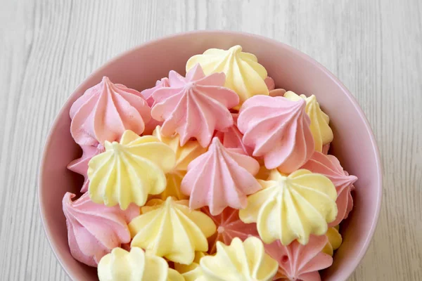 Mini meringues Beyaz ahşap zemin, yan görünüm üzerinde pembe bir kase. Yakın çekim.