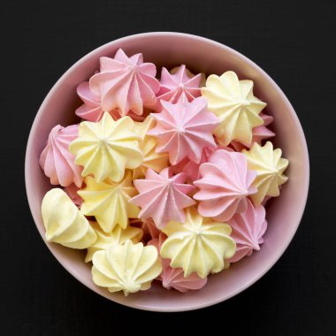 Mini meringues siyah arka plan, üstten görünüm üzerinde pembe bir kase. Yukarıdan, tepegöz, düz yatıyordu. Yakın çekim.