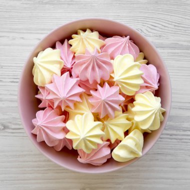 Beyaz ahşap yüzey üzerinde pembe bir kasede mini meringues yukarıdan görüntüleyin. Düz yatıyordu, genel gider, en iyi görünümü.