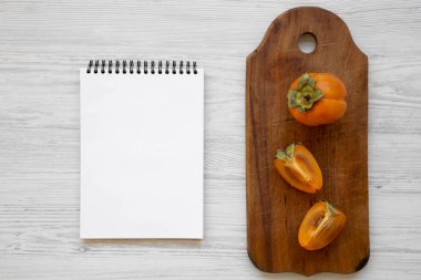 Taze hurma Doğrama tahtası, Beyaz ahşap arka plan, üstten görünüm üzerinde boş not defteri. Düz, tepegöz, yukarıdan yatıyordu.