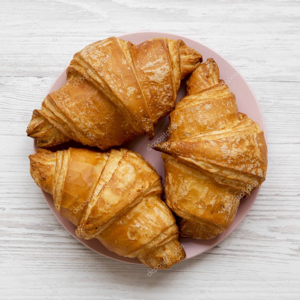 Fresh croissants with golden crust on white wooden table, overhead view. From above, flat lay.