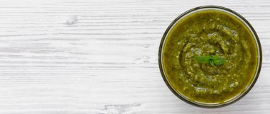 Beyaz ahşap arka planda, havai görünümü taze yapılmış fesleğen pesto kase. Yukarıdan Lay, düz. Kopya alanı.