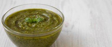 Beyaz ahşap arka planda, yan görünüm taze yapılmış fesleğen pesto kase. Portre. Kopya alanı.