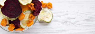 Sebze cips Beyaz ahşap zemin, havai görünümü üzerinde tam kase. Yukarıdan, lay düz. Metin için yer.