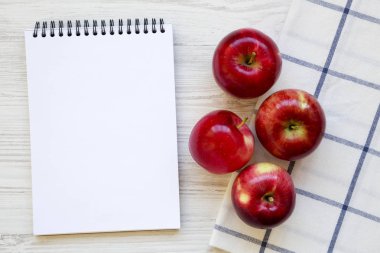 Taze çiğ kırmızı elma ve beyaz ahşap arka planda, havai görünümü boş not defteri. Yukarıdan, üstten görünüm düz yatıyordu. Metin için yer.