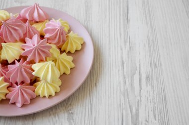 Mini meringues Beyaz ahşap bir masa düşük açılı görünümü üzerinde pembe plaka üzerinde. Yakın çekim. Kopya alanı.
