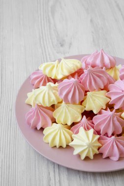Mini meringues Beyaz ahşap arka plan, düşük açılı görünümü üzerinde pembe plaka üzerinde. Portre.