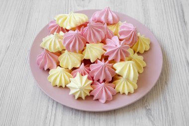 Mini meringues Beyaz ahşap zemin, düşük açılı görünümü üzerinde pembe plaka üzerinde. Yakın çekim.