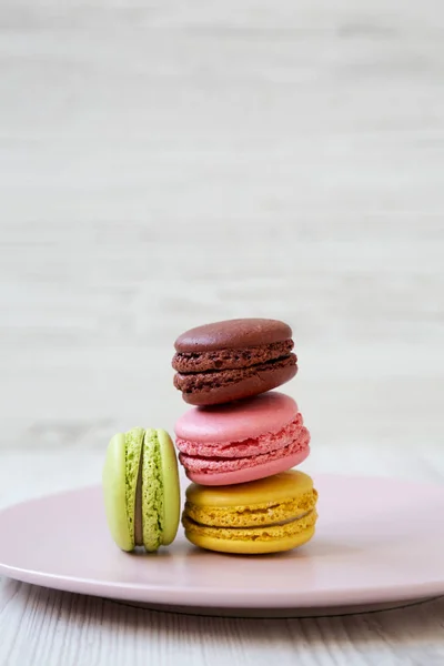 Sweet and colorful macaroons on pink plate on a white wooden background, side view. Close-up.