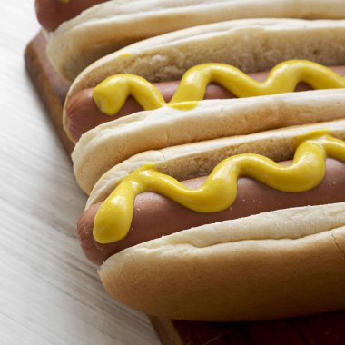 Beyaz ahşap masa, ahşap tahta üzerinde sarı hardallı Hotdog yakın çekim.