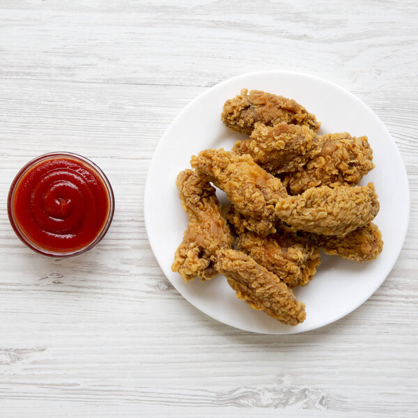 Куриные крылышки на круглой белой тарелке с красным перцовым соусом на белом деревянном фоне, вид сверху. Сверху, плоский, над головой
.