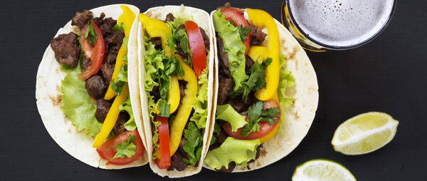 Mexican tacos with beef and vegetables, beer and lime on a dark background, overhead view. Flat lay, top view, from above.