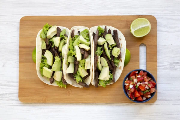 Mısır ekmeği ızgara sığır eti, avokado, kireç ve salsa Bambu tahta, üstten görünüm üzerinde. Yukarıda, ek yükü.