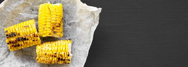 Grilled corn on the cob over black background, overhead view. Summer food. From above, flat lay. Space for text.
