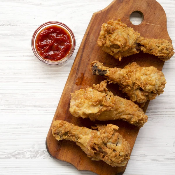 Fried chicken drumsticks with sauce on wooden board over white wooden background, top view. Overhead, flat lay, from above.