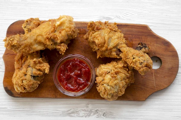 Fried chicken drumsticks with sauce on wooden board over white wooden surface, overhead view. Flat lay, from above, top view.