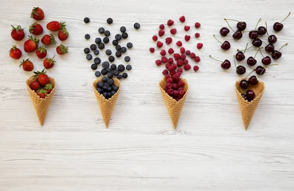 华夫甜冰淇淋锥与覆盆子 草莓和蓝莓在白色的木质表面 顶视图 从上面 — 图库照片