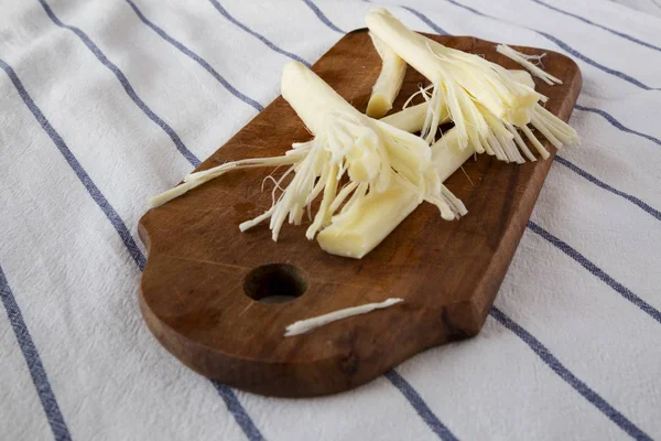 String cheese on rustic wooden board on cloth, side view. Healthy snack. Close-up.