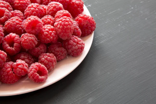 Taze organik ahududu siyah yüzey, düşük açılı görünüş üzerinde pembe bir tabakta. Yakın çekim. Kopya alanı.