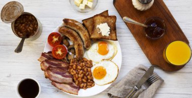 Tam İngiliz kahvaltısı kızarmış yumurta, pastırma, sosis, fasulye ve tost Beyaz ahşap yüzey, en iyi görünüm ile. Yukarıdaki üzerinden düz lay.