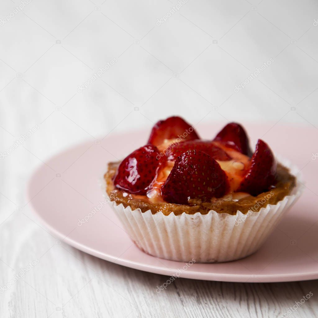 Strawberry vanilla cream cheese tart on pink plate, side view. Close-up. White wooden background.
