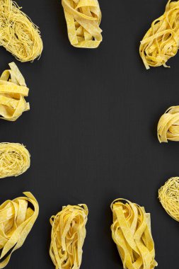 Siyah arka plan, üstten görünüm üzerinde çeşitli pişmemiş makarna (fettuccine, pappardelle, tagliolini) kümesi. Yukarıdan Lay, düz. Kopya alanı.