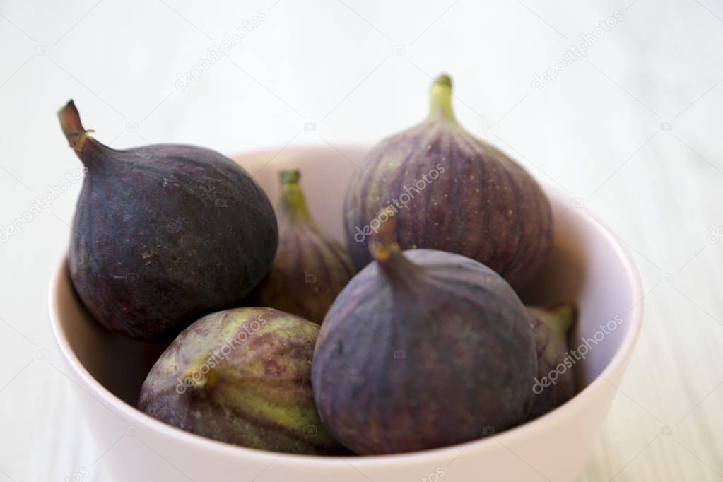 Fresh figs in a pink bowl on a white wooden background, side view. Closeup. Selective focus.