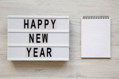 Metin 'Happy new year' ve beyaz ahşap arka plan, üstten görünüm üzerinde boş not defteri ile modern yönetim kurulu. Tepegöz, lay, yukarıdan düz. 2019