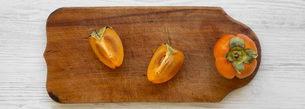 Fresh persimmon on a rustic wooden board over white wooden background, overhead view. Flat lay, from above.