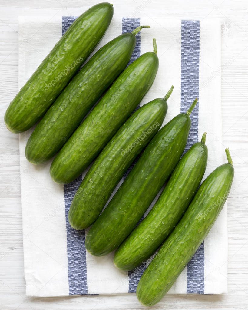 Fresh organic green cucumbers on cloth on a white wooden background, overhead view. Flat lay, from above, top view. Closeup.