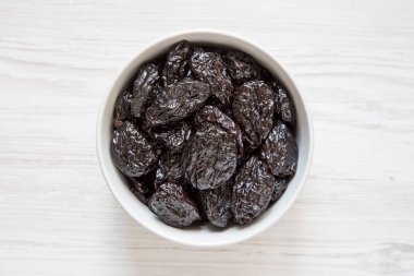 Beyaz ahşap yüzey, en iyi görünüm üzerinde kuru kuru erik tam kase. Tepegöz, yukarıdan lay, düz.