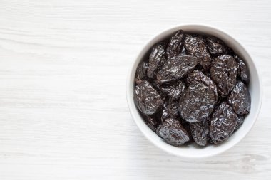 Beyaz ahşap zemin, üstten görünüm üzerinde kuru kuru erik tam kase. Tepegöz, lay, yukarıdan düz. Kopya alanı.