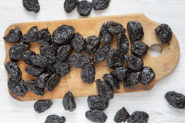 Beyaz ahşap zemin, havai görünümü üzerinde rustik ahşap tahta üzerinde kuru erik. Yukarıdan, üstten görünüm düz lay.