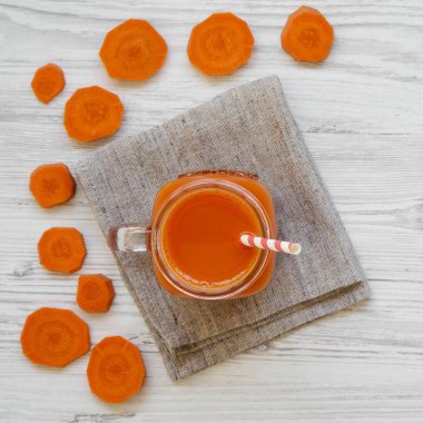 Cam sürahi taze havuç güler yüzlü beyaz tahta yüzeyi, havai görünümü. Yat, yukarıdan görünüm, top. Yakın çekim.