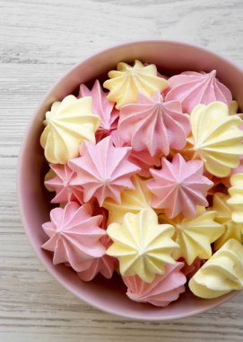 Mini meringues Beyaz ahşap arka plan, üstten görünüm üzerinde pembe bir kase. Düz, tepegöz, yukarıdan yatıyordu. Yakın çekim.
