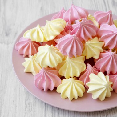 Beyaz ahşap yüzey, yan görünüm üzerinde pembe plaka üzerinde mini meringues. 