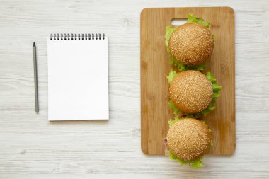 Çizburger ve beyaz ahşap arka planda, havai görünümü boş not defteri. Yukarıdan Lay, düz. Metin için yer.