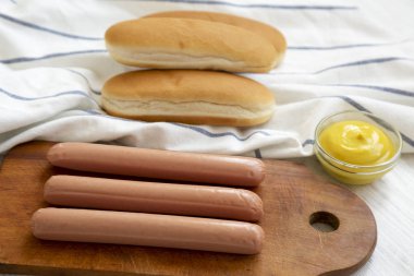 Sosisli sandviç yapmak için malzemeler: sosis, sosisli ekmeği ve hardal beyaz ahşap arka planda, yan görünüm. Portre.