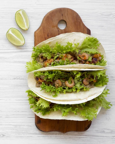 Shrimp tacos on wooden board on white wooden surface, top view. Mexican cuisine. Flat lay, from above, overhead.