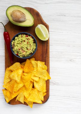 Beyaz ahşap zemin, ek yükü üzerinde rustik ahşap tahta üzerinde cips ile geleneksel Meksika guacamole kase. Üstten görünüm. Kopya alanı.