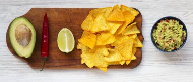 Geleneksel Meksika guacamole kase ve cips Beyaz ahşap zemin, ek yükü üzerine ahşap tahta üzerinde malzemelerle. Yukarıdan. Üstten görünüm. 
