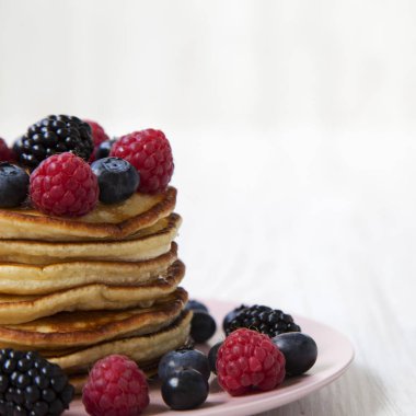 Beyaz ahşap arka plan, yan görünüm üzerinde pembe bir plaka üzerinde çilek ile krep. Kopya alanı.