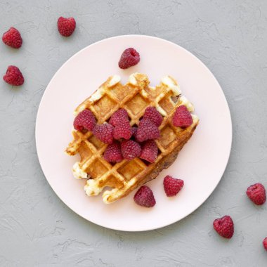 Ahududu gri arka plan, üstten görünüm üzerinde pembe plaka ile geleneksel Belçika waffle. Yukarıdan Lay, düz. Yakın çekim.