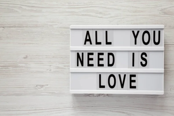 Lightbox with text 'All you need is love' over white wooden surface, top view. From above, flat lay, overhead.