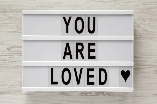 Stock image Modern board with text 'You are loved' on a white wooden surface, top view. Flat lay, overhead. Closeup.