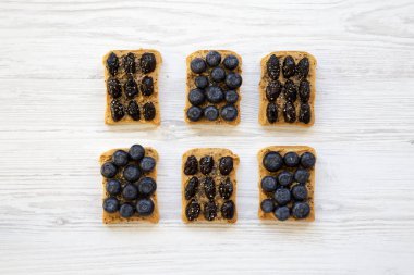 Fıstık ezmesi, yaban mersini, zeytin ve beyaz ahşap bir masa üstten görünüm üzerinde chia tohum ile Vegan tost. Sağlıklı beslenme. Yukarıdaki üzerinden düz lay. 