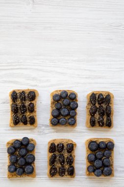 Fıstık ezmesi, yaban mersini, zeytin ve beyaz tahta yüzeyi, havai görünümü chia tohum ile Vegan tost. Sağlıklı beslenme. Yukarıdan Lay, düz. Kopya alanı.